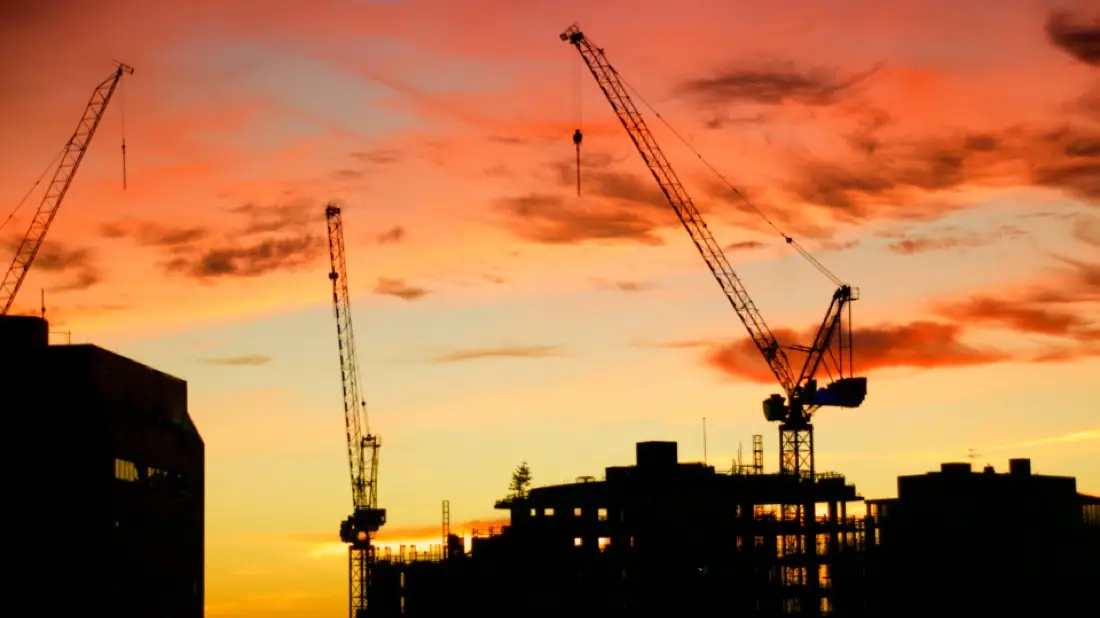 Construction cranes silhouetted against an orange sunset