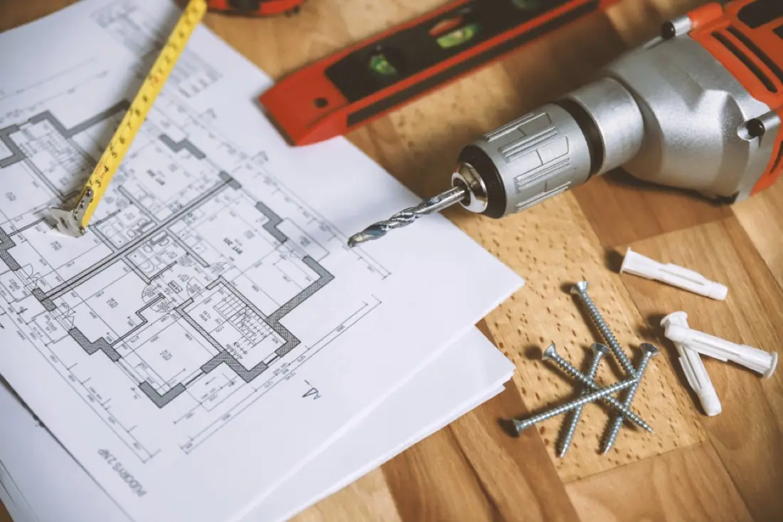 Architectural floor plan on a desk with measuring tape and drill