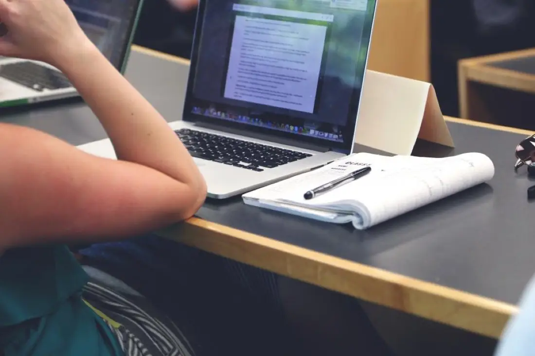 Student taking notes beside a laptop